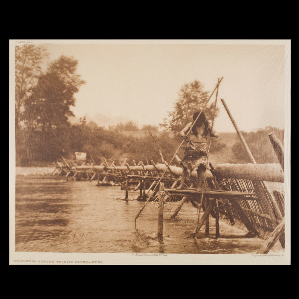 Photograph of young Native American girl standing on a fishing weir that spans a river.