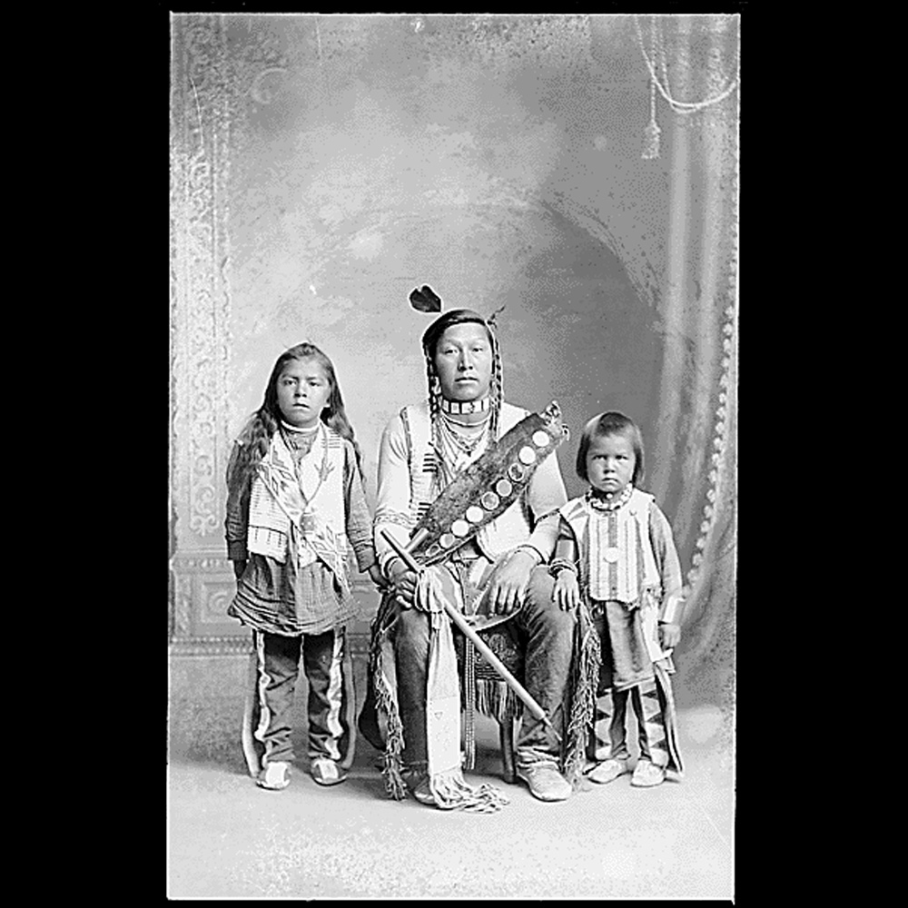 Photograph of an adult and two children of the Northern Shoshone tribe in traditional dress.