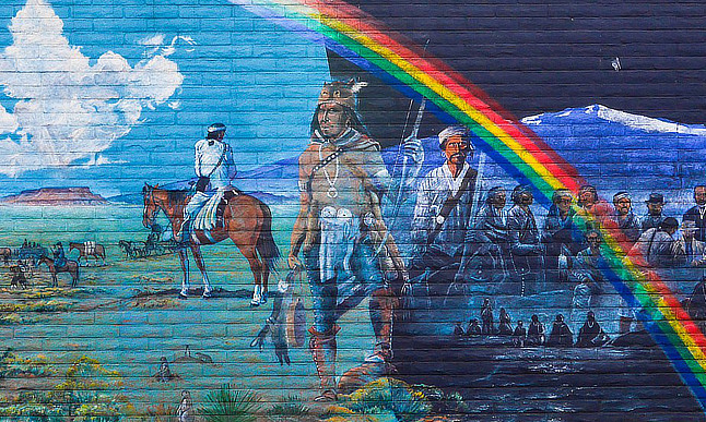 Mural of Native Americans traveling over a landscape beneath a rainbow.